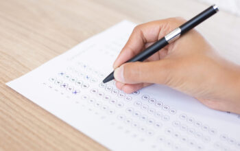 Closeup of hand holding pen and filling out questionary form on table