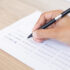 Closeup of hand holding pen and filling out questionary form on table